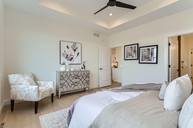 bedroom featuring light wood-type flooring, a tray ceiling, and ceiling fan