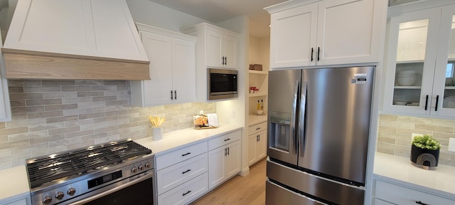 kitchen featuring white cabinetry, decorative backsplash, custom exhaust hood, and appliances with stainless steel finishes