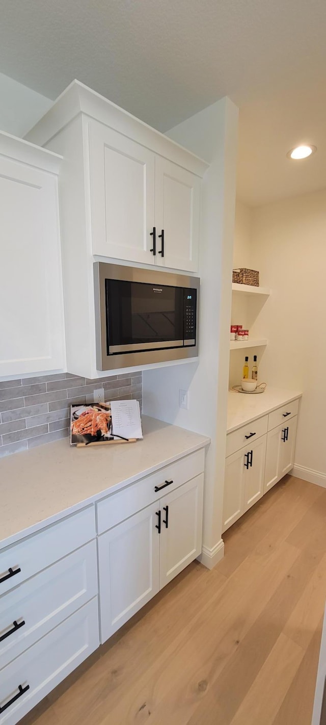 bar with white cabinetry, stainless steel microwave, and light hardwood / wood-style floors