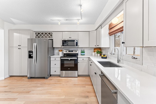 kitchen featuring appliances with stainless steel finishes, tasteful backsplash, sink, light hardwood / wood-style floors, and a textured ceiling