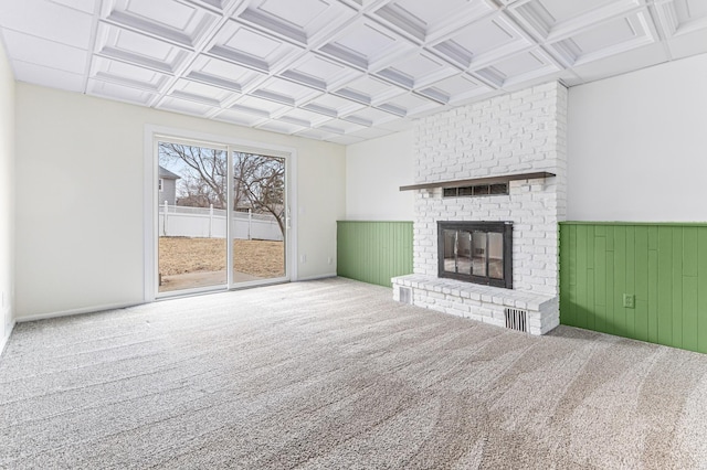 unfurnished living room featuring coffered ceiling, a brick fireplace, carpet flooring, and wooden walls