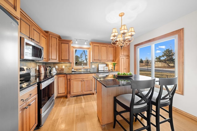 kitchen with decorative light fixtures, decorative backsplash, a kitchen island, a notable chandelier, and appliances with stainless steel finishes