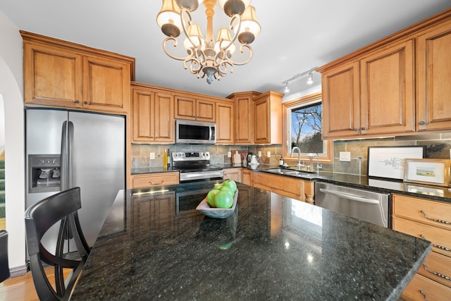 kitchen featuring dark stone countertops, stainless steel appliances, pendant lighting, sink, and an inviting chandelier