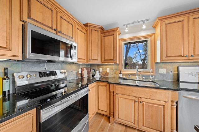 kitchen featuring dark stone countertops, appliances with stainless steel finishes, light wood-type flooring, sink, and tasteful backsplash