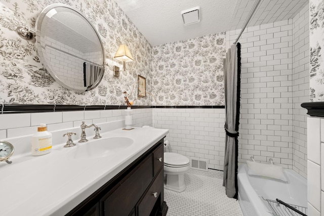 full bathroom with a textured ceiling, tile walls, tile patterned floors, vanity, and tiled shower / bath combo