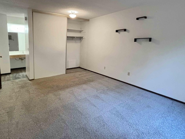 unfurnished bedroom featuring carpet, ensuite bathroom, a textured ceiling, and a closet