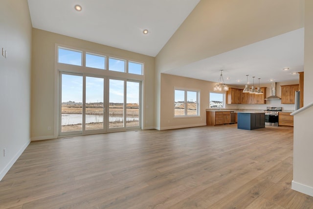 unfurnished living room with high vaulted ceiling, a water view, sink, light wood-type flooring, and a chandelier