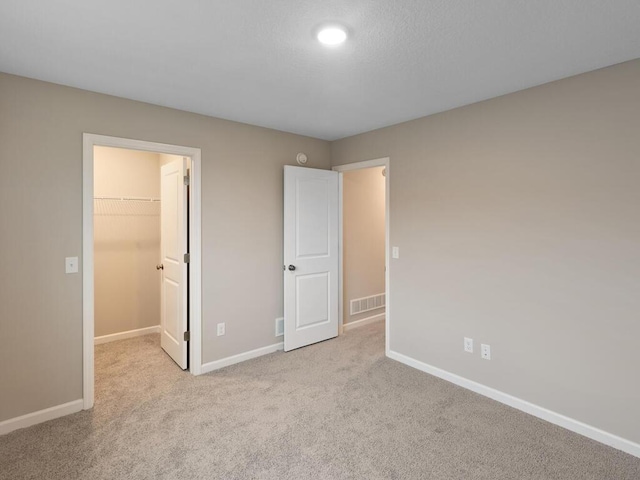 unfurnished bedroom featuring light colored carpet, a walk in closet, and a closet