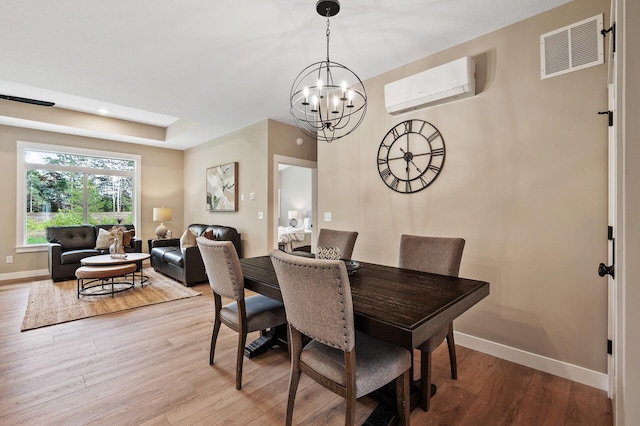 dining area featuring a raised ceiling, light hardwood / wood-style floors, a wall unit AC, and a notable chandelier