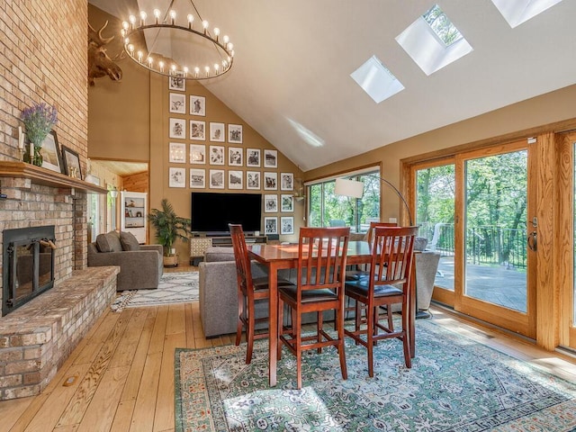 dining space featuring a fireplace, vaulted ceiling with skylight, a chandelier, and light wood-type flooring