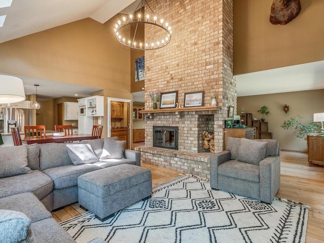 living room with an inviting chandelier, a fireplace, high vaulted ceiling, and light hardwood / wood-style floors