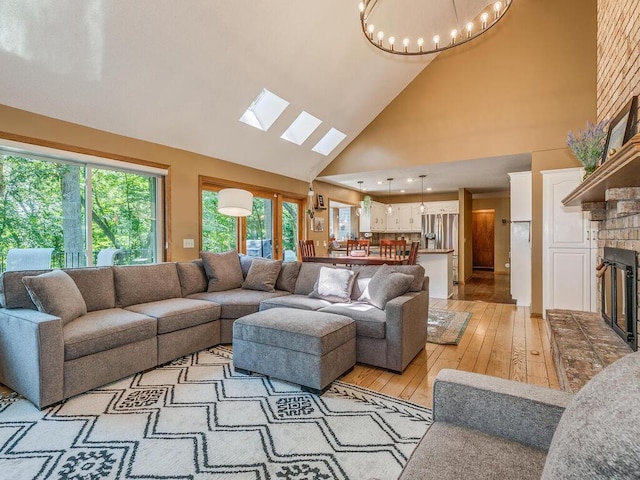 living room with a brick fireplace, a notable chandelier, high vaulted ceiling, and light hardwood / wood-style flooring