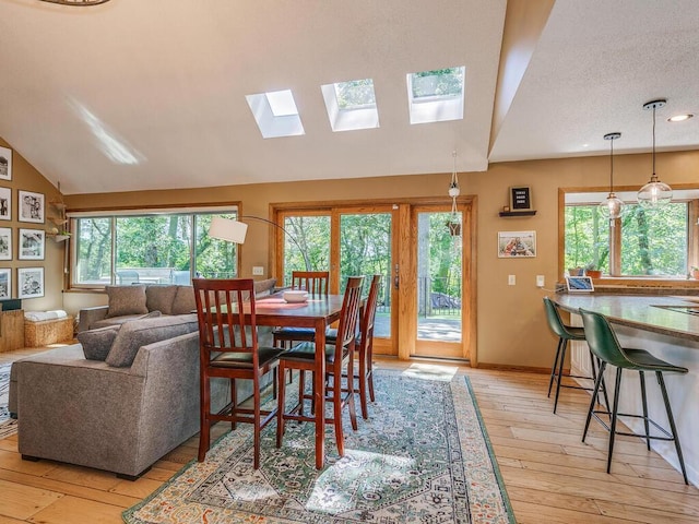 dining room with lofted ceiling with skylight, a healthy amount of sunlight, and light wood-type flooring