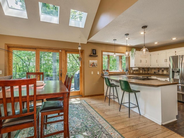 kitchen with stainless steel fridge with ice dispenser, tasteful backsplash, white cabinetry, hanging light fixtures, and kitchen peninsula