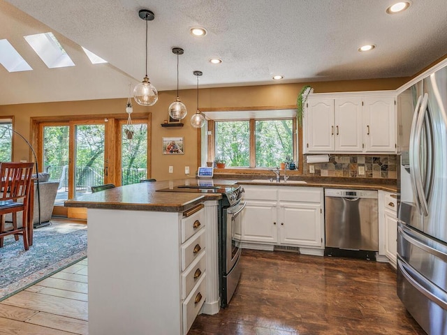 kitchen with pendant lighting, white cabinetry, a skylight, stainless steel appliances, and kitchen peninsula