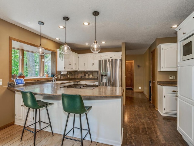 kitchen with sink, stainless steel fridge, white microwave, decorative backsplash, and white cabinets