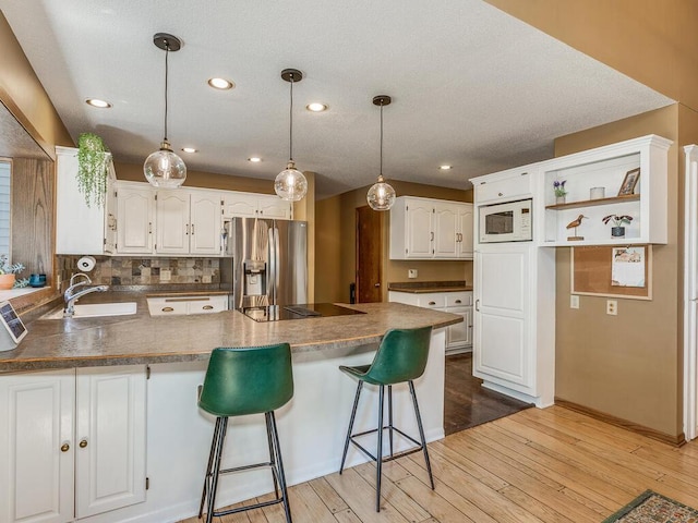 kitchen with sink, white cabinetry, white microwave, stainless steel refrigerator with ice dispenser, and black electric cooktop