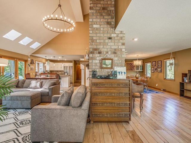 living room with high vaulted ceiling, a notable chandelier, light wood-type flooring, and a skylight