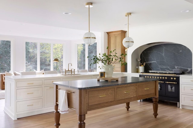 kitchen with backsplash, double oven range, light wood-type flooring, hanging light fixtures, and a sink