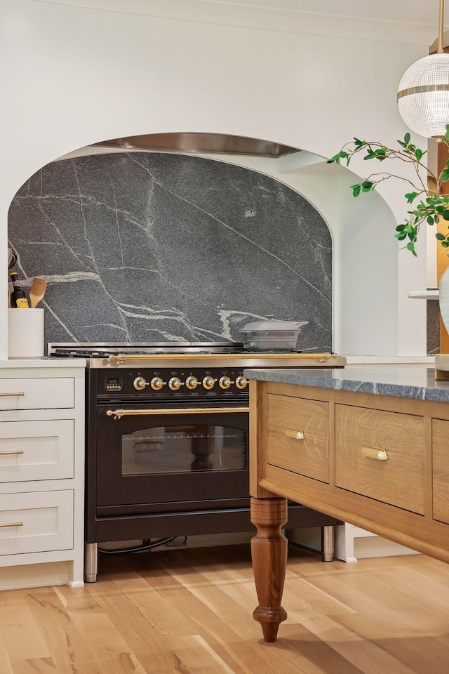 kitchen with decorative light fixtures, high end stove, light wood-type flooring, and decorative backsplash