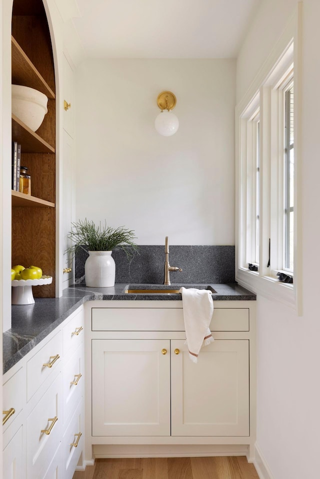 kitchen with dark stone counters, a wealth of natural light, sink, and white cabinets