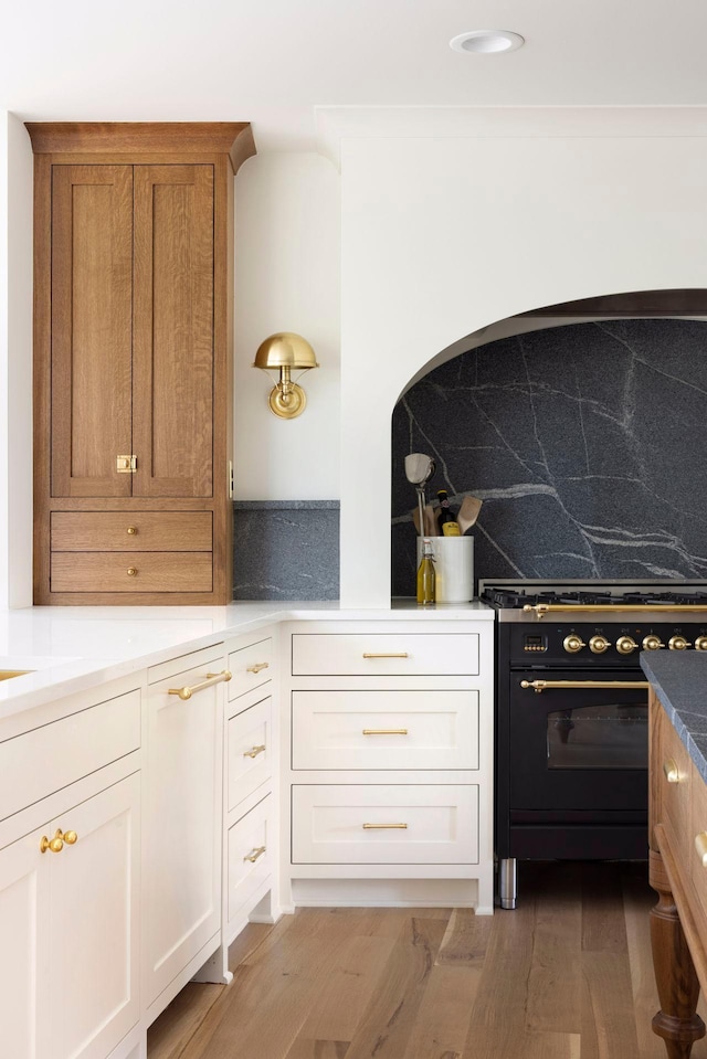 kitchen featuring tasteful backsplash, light hardwood / wood-style flooring, high end stove, and white cabinets