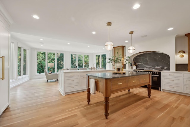 kitchen with white cabinetry, decorative light fixtures, high end stove, and a kitchen island