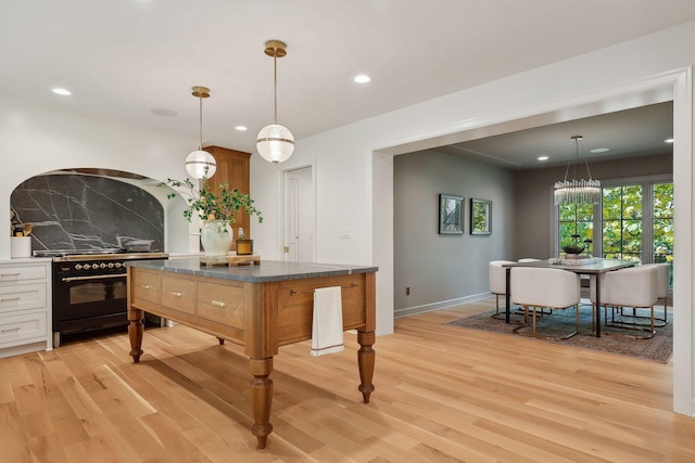 kitchen with decorative light fixtures, backsplash, light wood-type flooring, and high end stove