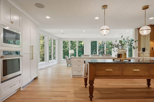 kitchen featuring white cabinetry, hanging light fixtures, oven, and dark stone counters