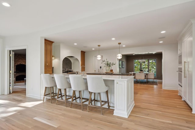 kitchen featuring a kitchen bar, light hardwood / wood-style flooring, kitchen peninsula, pendant lighting, and white cabinets