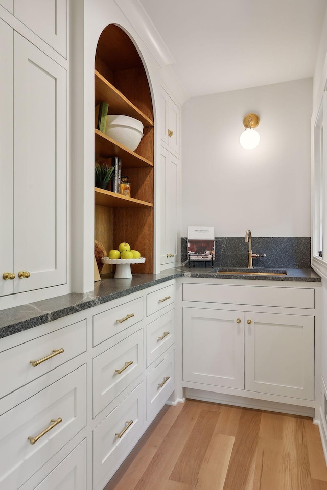 interior space with light wood-type flooring, dark stone counters, sink, and white cabinets