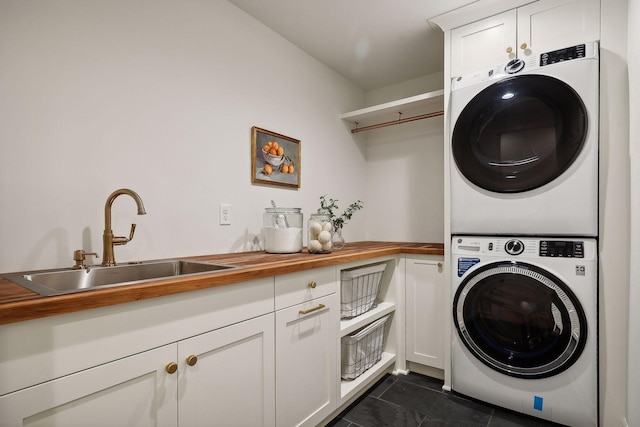 laundry room featuring sink, cabinets, dark tile patterned floors, and stacked washer / dryer