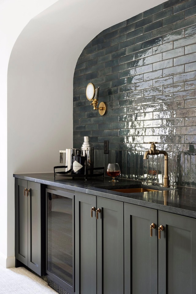 bar featuring dark stone countertops, brick wall, gray cabinetry, and beverage cooler