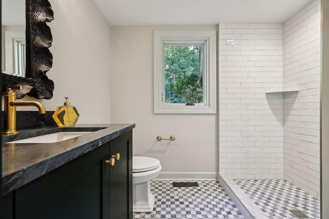 bathroom with tiled shower, vanity, and toilet