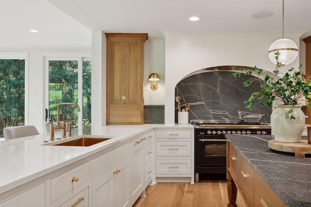 kitchen featuring light wood finished floors, range with two ovens, recessed lighting, a sink, and decorative backsplash