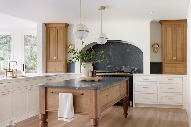 kitchen with tasteful backsplash, light wood finished floors, dark countertops, hanging light fixtures, and a sink