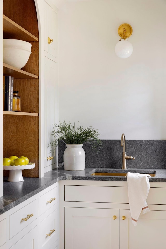 interior space with a sink, arched walkways, dark countertops, and white cabinetry