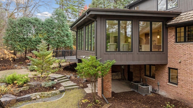 view of side of property with brick siding, board and batten siding, central AC, a sunroom, and a patio area