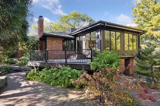 back of house with a deck, brick siding, a sunroom, and a chimney