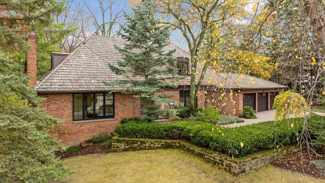 view of front facade featuring brick siding, driveway, a chimney, and a garage