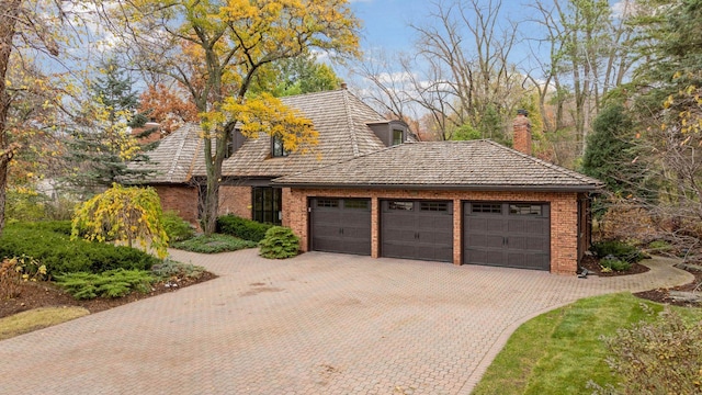 view of front of home featuring decorative driveway, brick siding, an attached garage, and a chimney