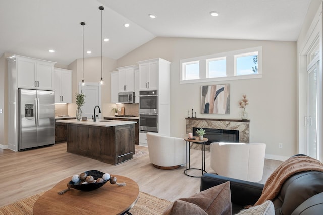 kitchen with decorative backsplash, stainless steel appliances, pendant lighting, light hardwood / wood-style flooring, and an island with sink