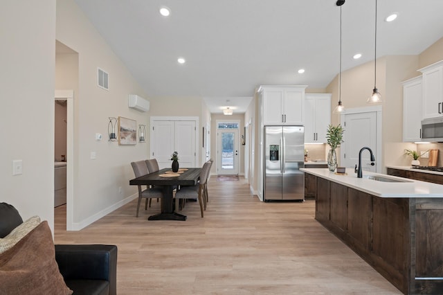 kitchen featuring a kitchen island with sink, sink, hanging light fixtures, light hardwood / wood-style flooring, and stainless steel appliances