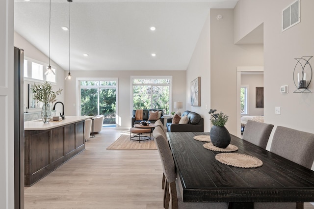 dining space featuring high vaulted ceiling and light hardwood / wood-style flooring