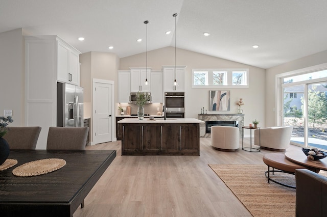 kitchen featuring a center island with sink, hanging light fixtures, light hardwood / wood-style flooring, a premium fireplace, and stainless steel appliances