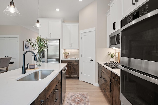 kitchen featuring white cabinetry, sink, hanging light fixtures, stainless steel appliances, and dark brown cabinets