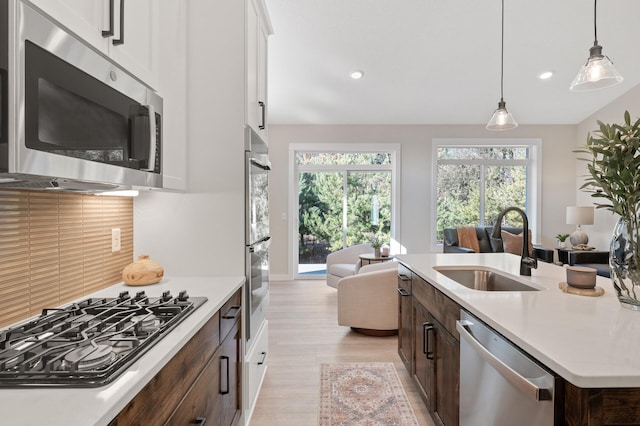 kitchen featuring appliances with stainless steel finishes, dark brown cabinetry, sink, white cabinets, and an island with sink