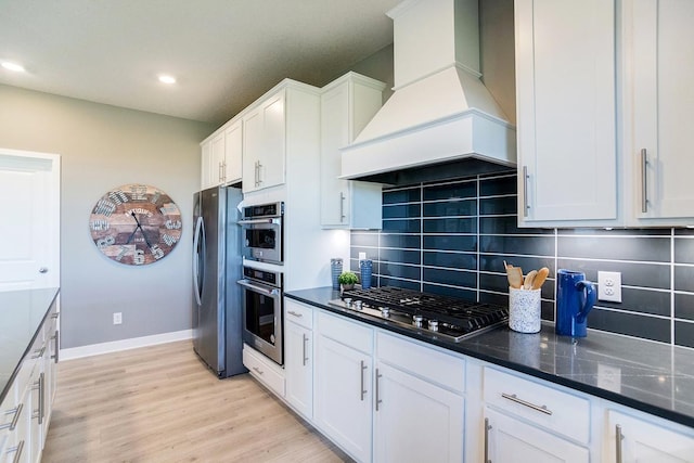 kitchen featuring decorative backsplash, appliances with stainless steel finishes, light wood-type flooring, premium range hood, and white cabinetry