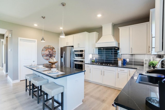 kitchen featuring premium range hood, a kitchen bar, light wood-type flooring, stainless steel appliances, and decorative backsplash