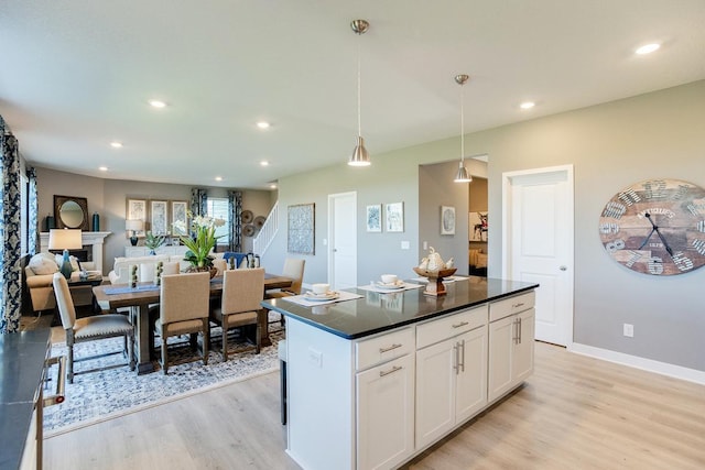 kitchen with dark countertops, a center island, white cabinetry, light wood-style floors, and hanging light fixtures